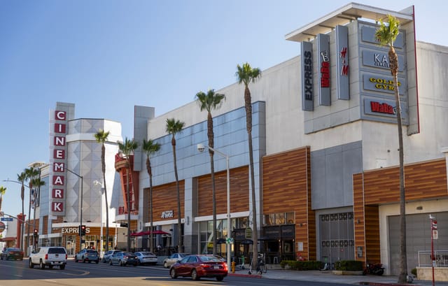 Cars drive by a large retail shopping center and movie theater.