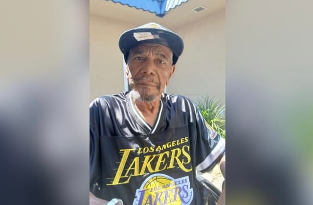 A man wearing a baseball cap and a dark Los Angeles Lakers jersey.