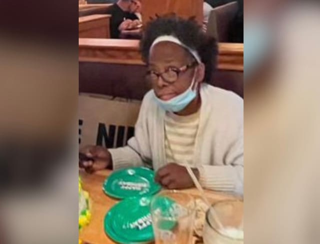 A woman with a surgical mask covering her chin sits at a table.