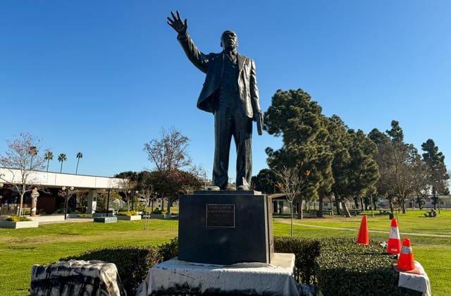 A statue of a man holding out his hand in the middle of a park under a clear blue sky.