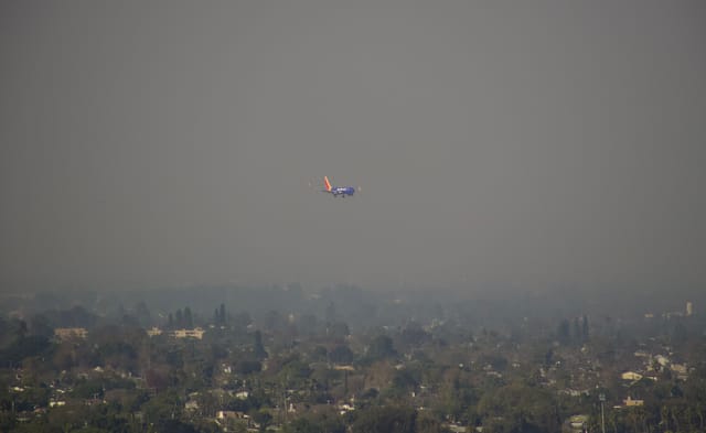 A plane flies though a murky brown sky.