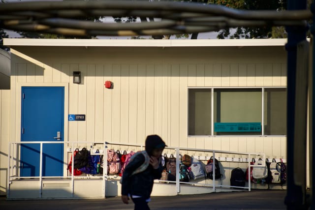 A child runs past a beige building with a blue door.