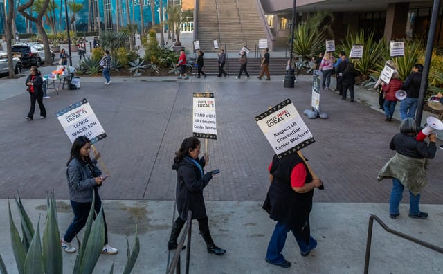 People walk in a circle holding signs that read "respect LB convention center workers."