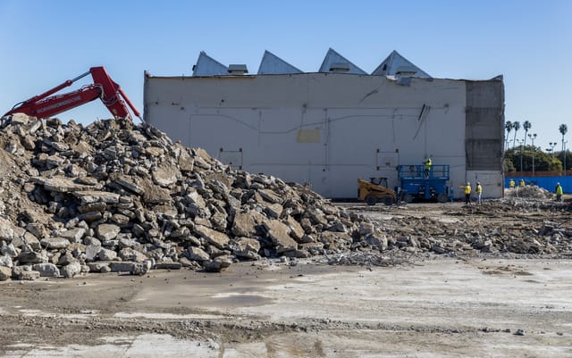 A pile of concrete rubble sits on the ground as crews demolish a building.