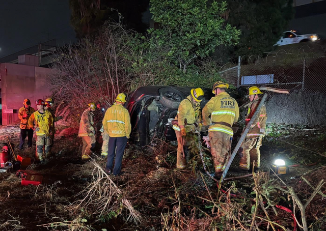 People in yellow jackets stand near an overturned car at night.