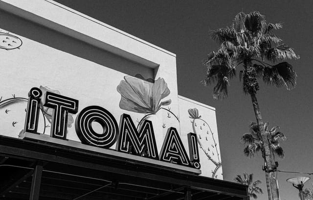 A sign on a building reads "Toma" beside a palm tree.