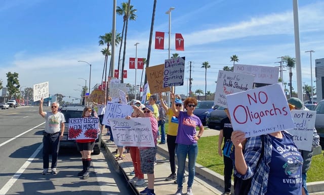 People waving signs in front of a Tesla dealership.