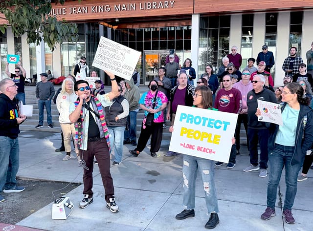 People stand and hold signs in front of a building displaying the sign "Billie Jean King Main Library."