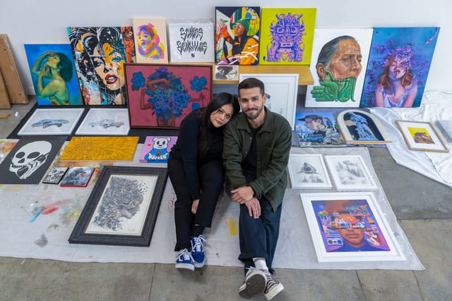 A man and woman sit on the floor surrounded by colorful works of art.