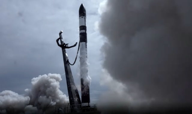 Smoke billows out from a black and white rocket as it blasts off.