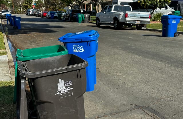 An empty black, green and blue trash can sit on the street.