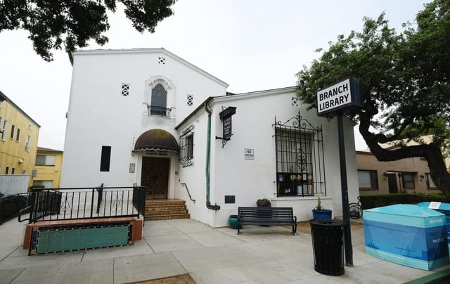 A white building with ornate black metal railings next to a sign saying "Branch Library.