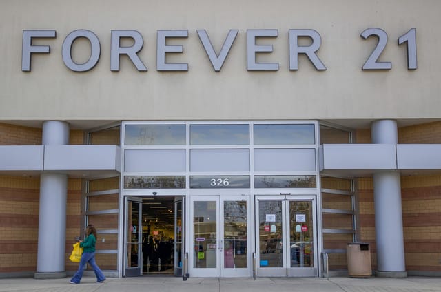 A woman in jeans and a green sweater walks out of a retail store.