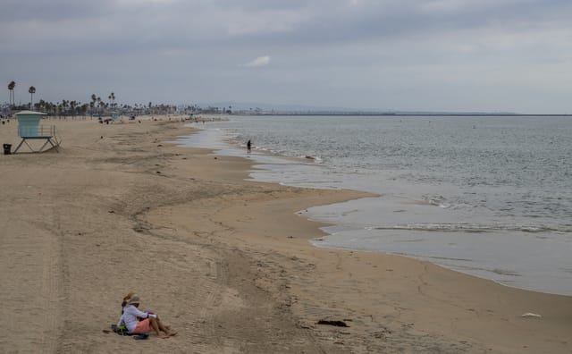 People sit on a beach on a cloudy day.