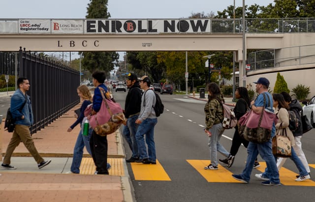 A group of people walk across a street with a sign in the background that reads "enroll now."