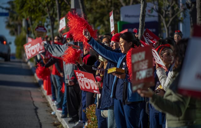 A long line of people wave red pom-poms and hold red and white signs that read "safe staffing now."