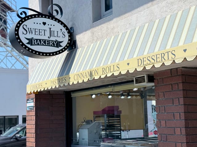 A brick and glass storefront labeled "Sweet Jill's Bakery."