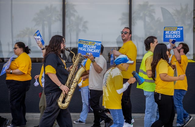 People wearing yellow shirts hold up signs and one saxophone.