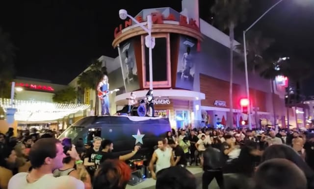 A crowd surrounds a band on a van at a street corner at night.
