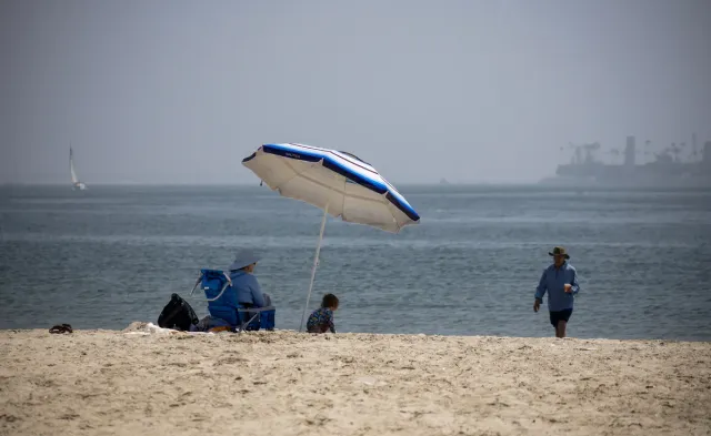People relax under an umbrella at the beach on a hazy day.