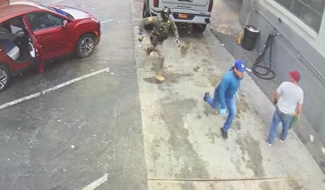 A masked man in camouflage chases a man in blue while another man watches them.