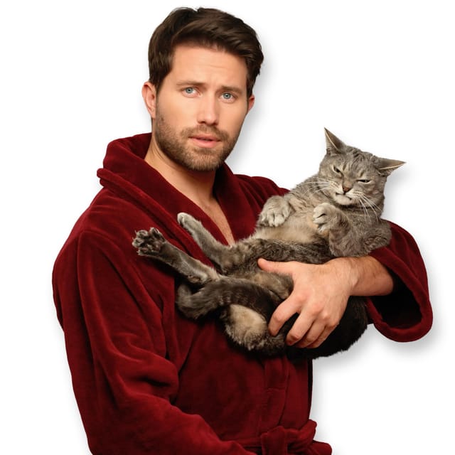 A man in a bathrobe holds a gray cat that is scowling.