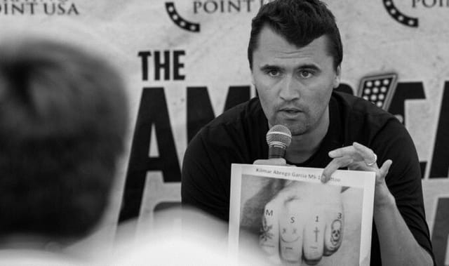 Black and white photo of a man holding a picture of a man's tattooed hand.