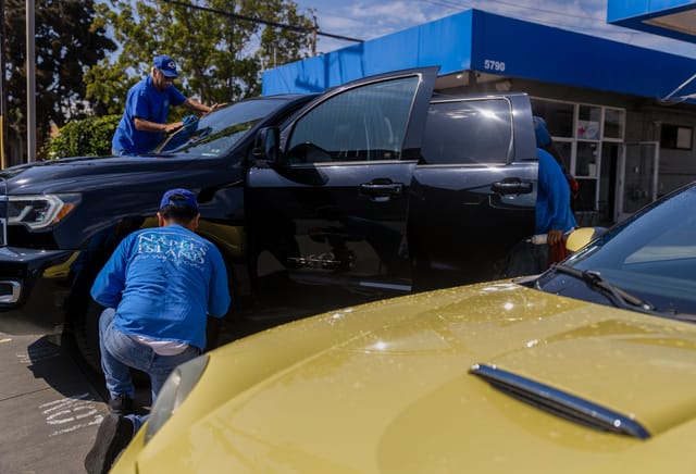 Three people wash a black truck with its doors open.