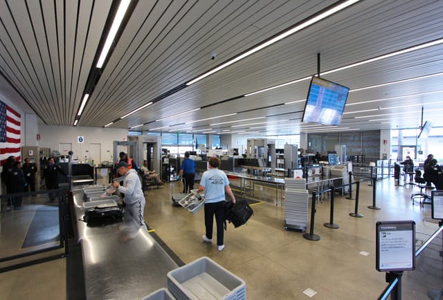 A small number of people standing at an airport security checkpoint. 