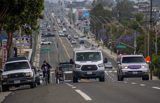 A person on a bike rides in the street alongside trucks.