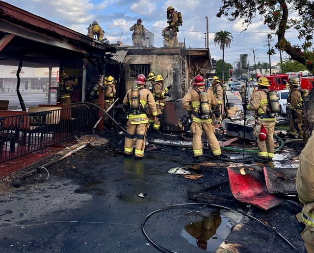 Firefighters stand near a burned out building.