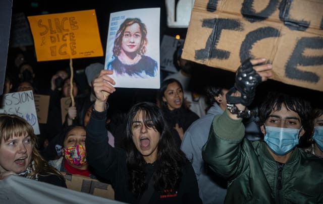 Dozens of people hold up signs protesting ICE at night.