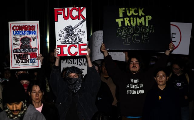 People at night hold signs saying slogans like "Fuck Ice" and "Fuck Trump Abolish Ice."