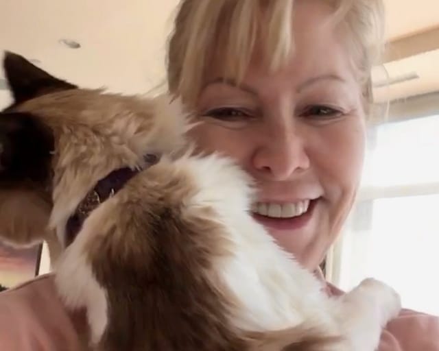A smiling woman hugs a fluffy cat close to her face.
