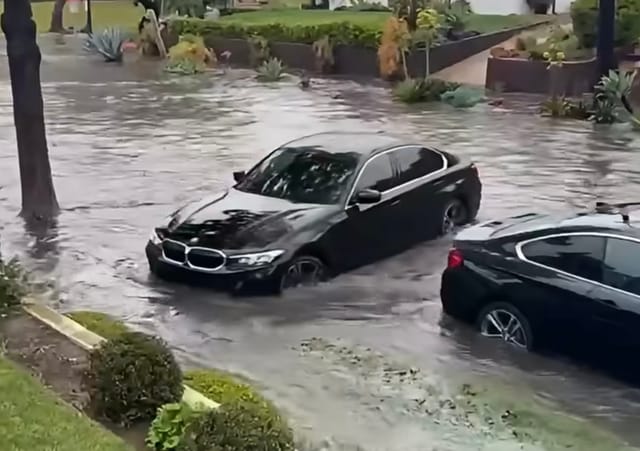 Two black cars sit in a flooded street.